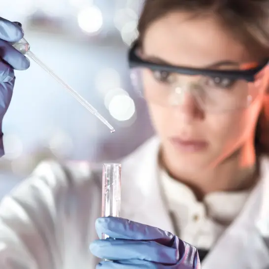 Scientist in a lab coat using a pipette to transfer liquid into a test tube, showcasing laboratory research and experimentation.